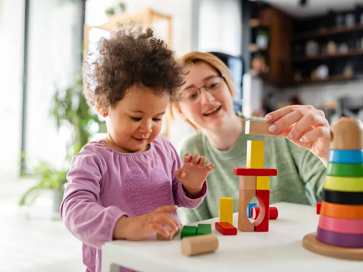 Eine Frau spielt mit einem kleinen Kind mit bunten Bauklötzen