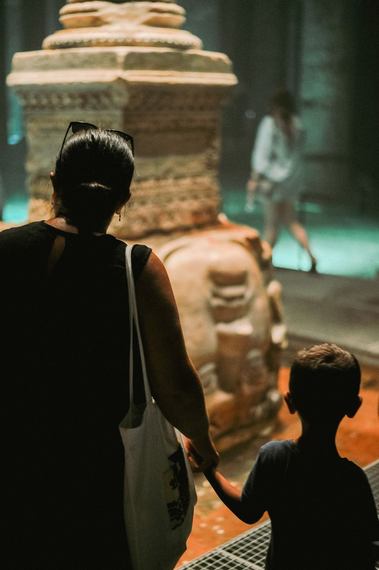 A mother and son hold hands as they explore a historical site indoors.