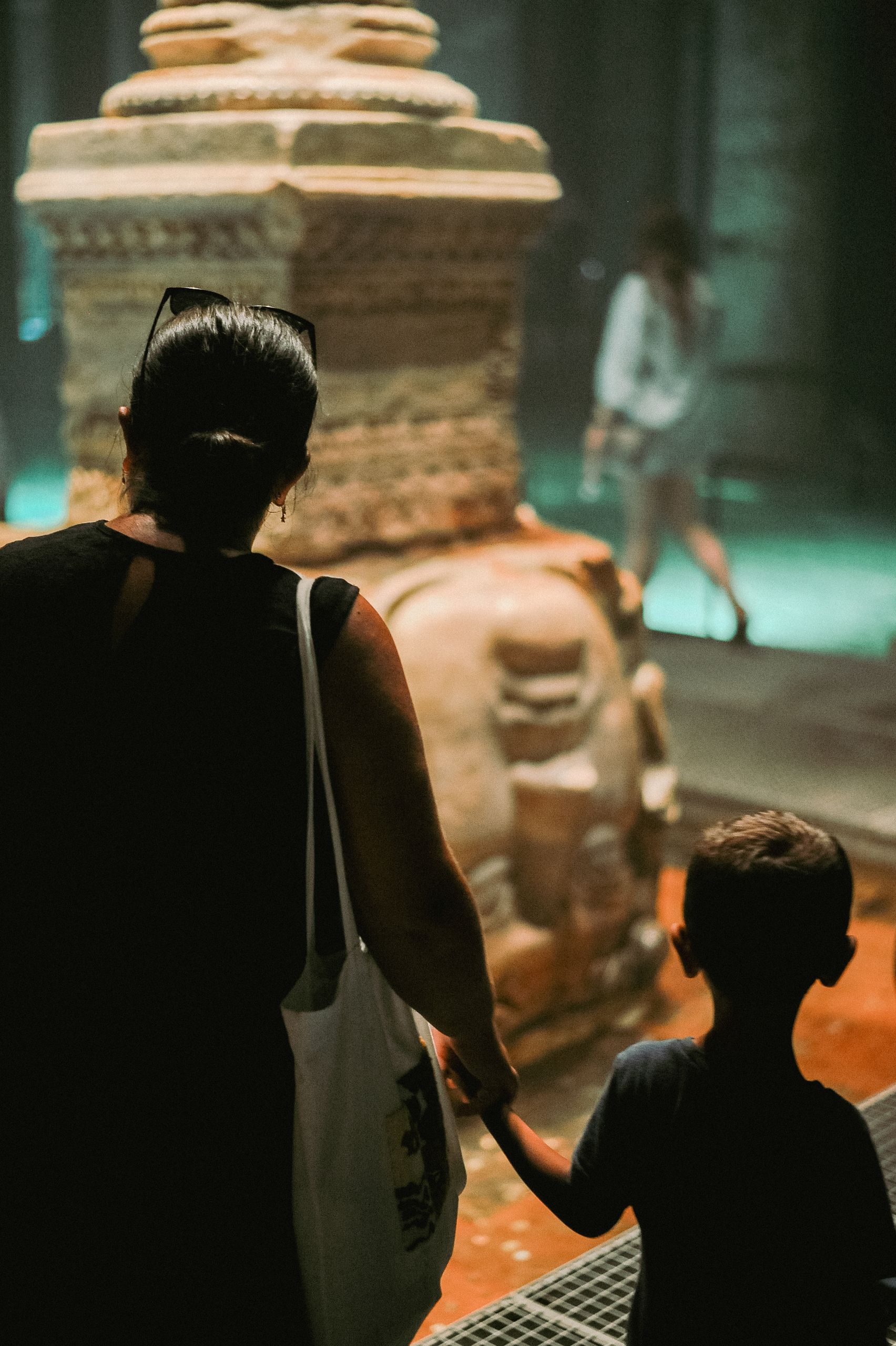 A mother and son hold hands as they explore a historical site indoors.